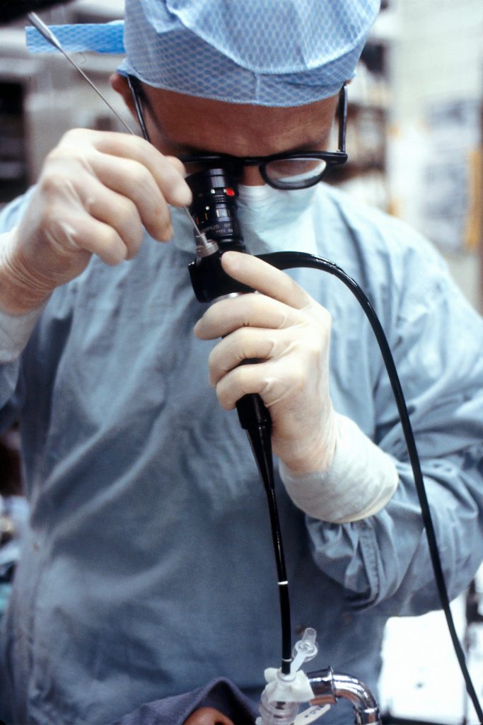 Photo by National Cancer Institute on Unsplash, shows a surgeon looking into a black, metallic tool, while a patient's nose is barely visible below.